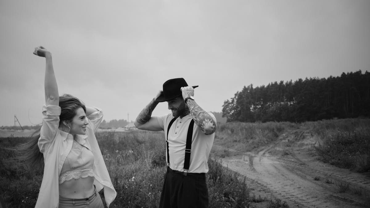 Couple in vintage fashion pose outdoors on a dirt road in black and white.